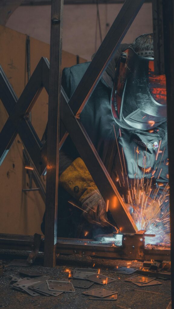 A welder wearing a mask in a workshop, creating sparks while welding metal.